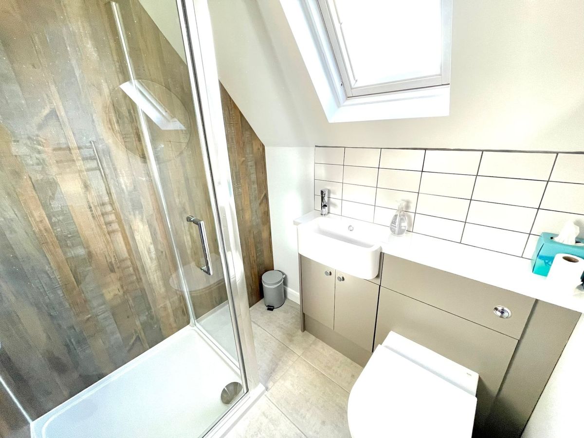 A shower room under a skylight with a glass shower enclosure, a grey vanity unit and white tiles